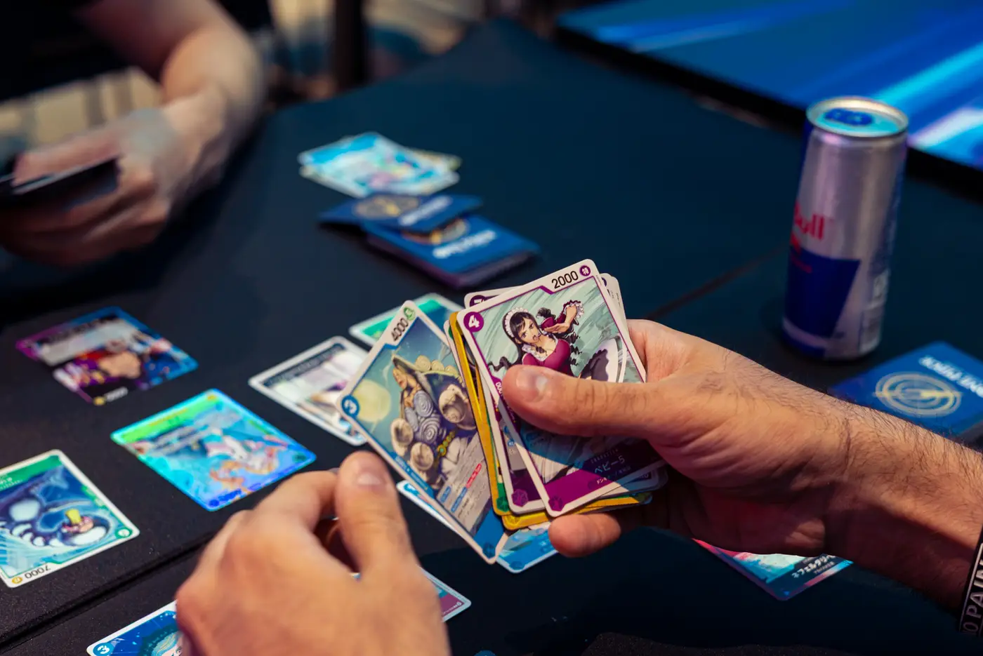 One-Piece-Karten auf der Hand, daneben eine Dose Red Bull